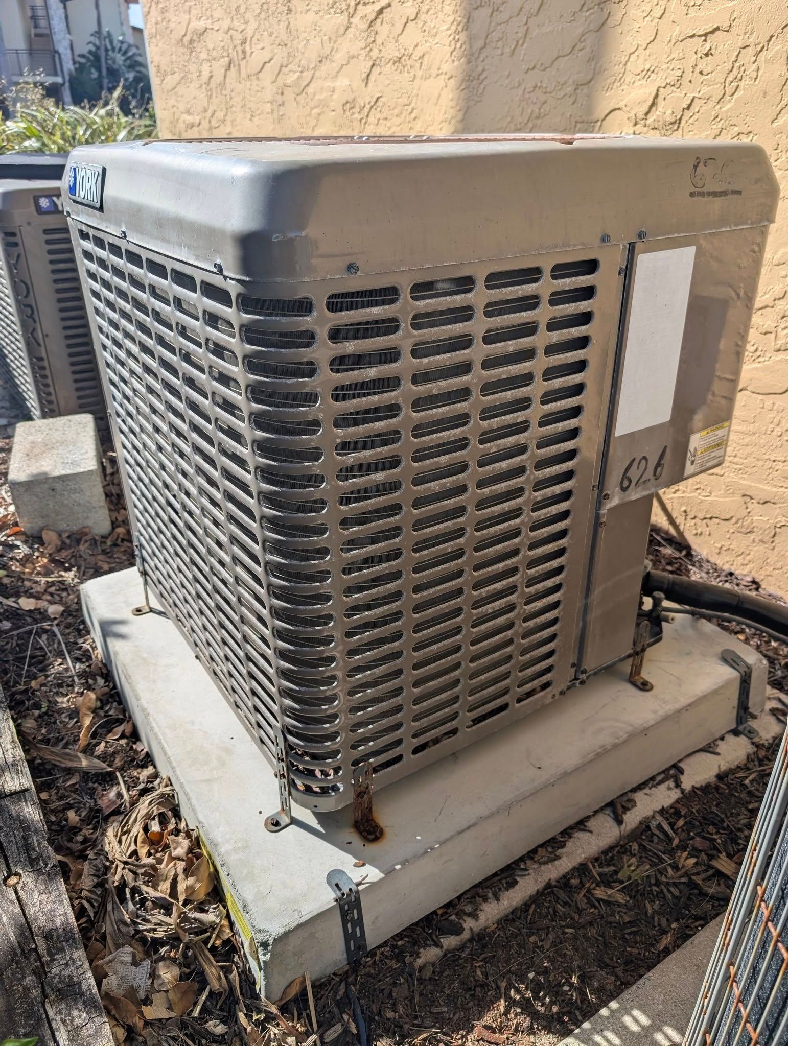 A silver air conditioner is sitting on top of a concrete block.