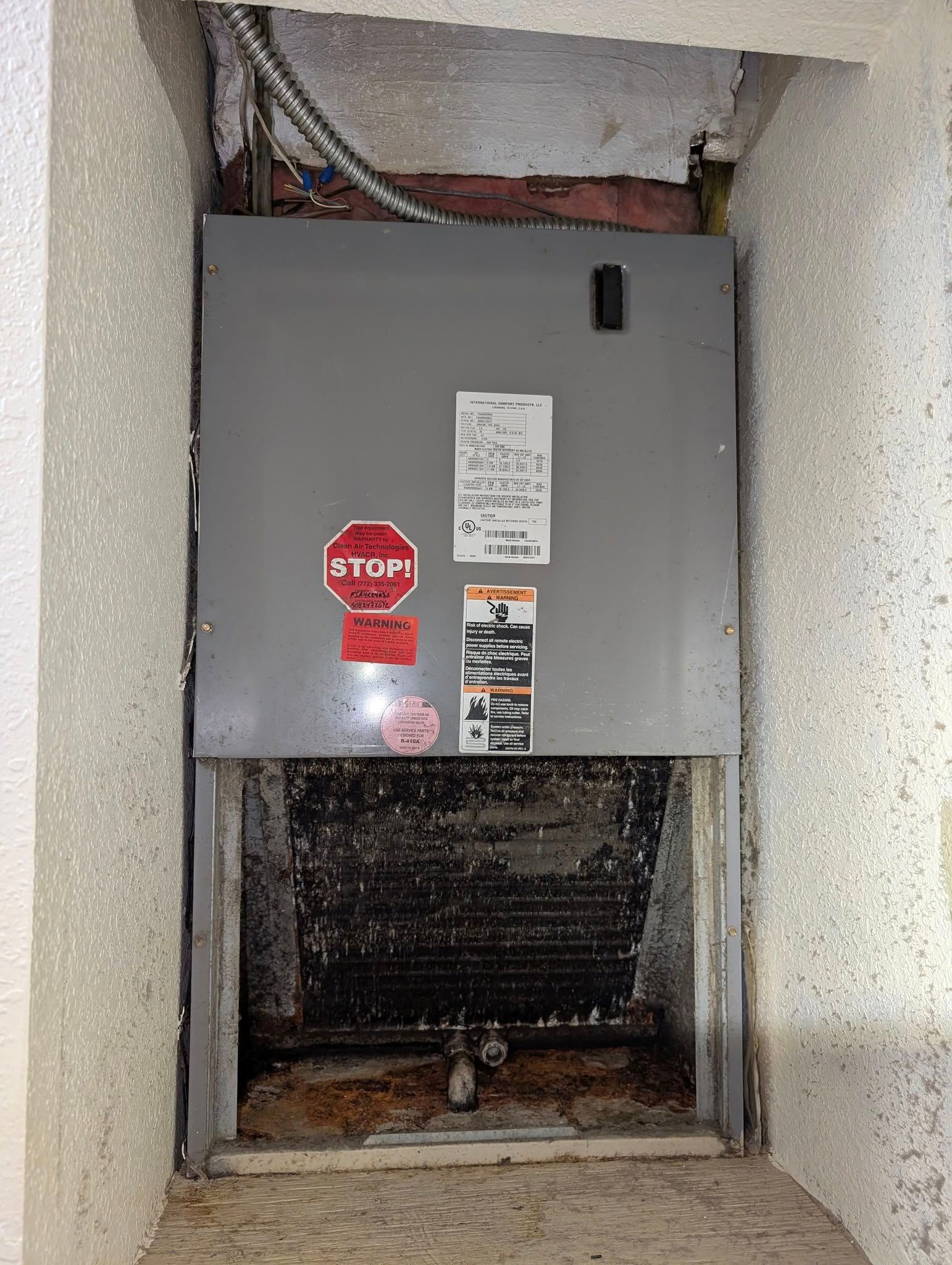 A dirty air conditioner is sitting in a corner of a room.