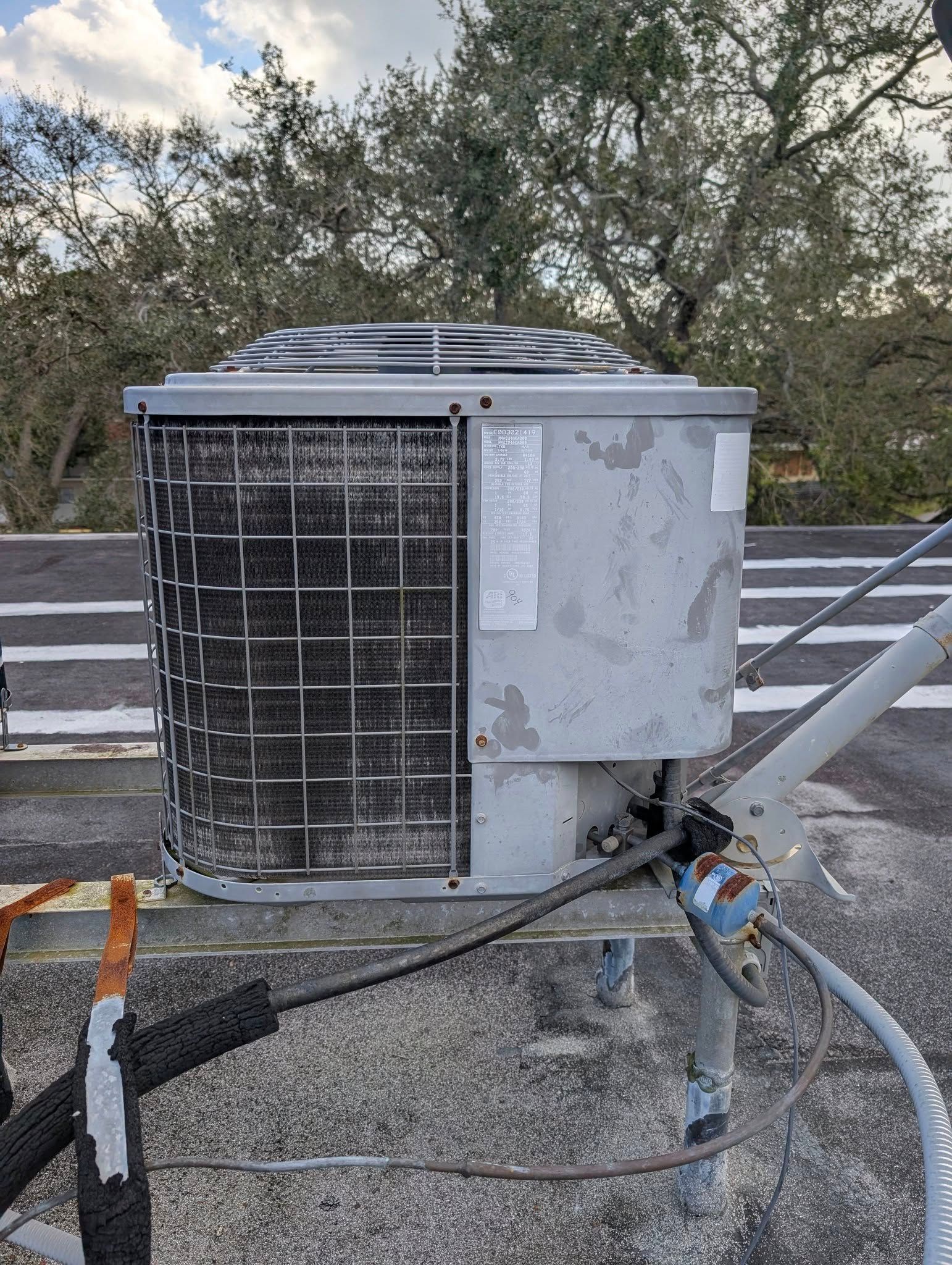 A dirty air conditioner is sitting on top of a roof next to a road.