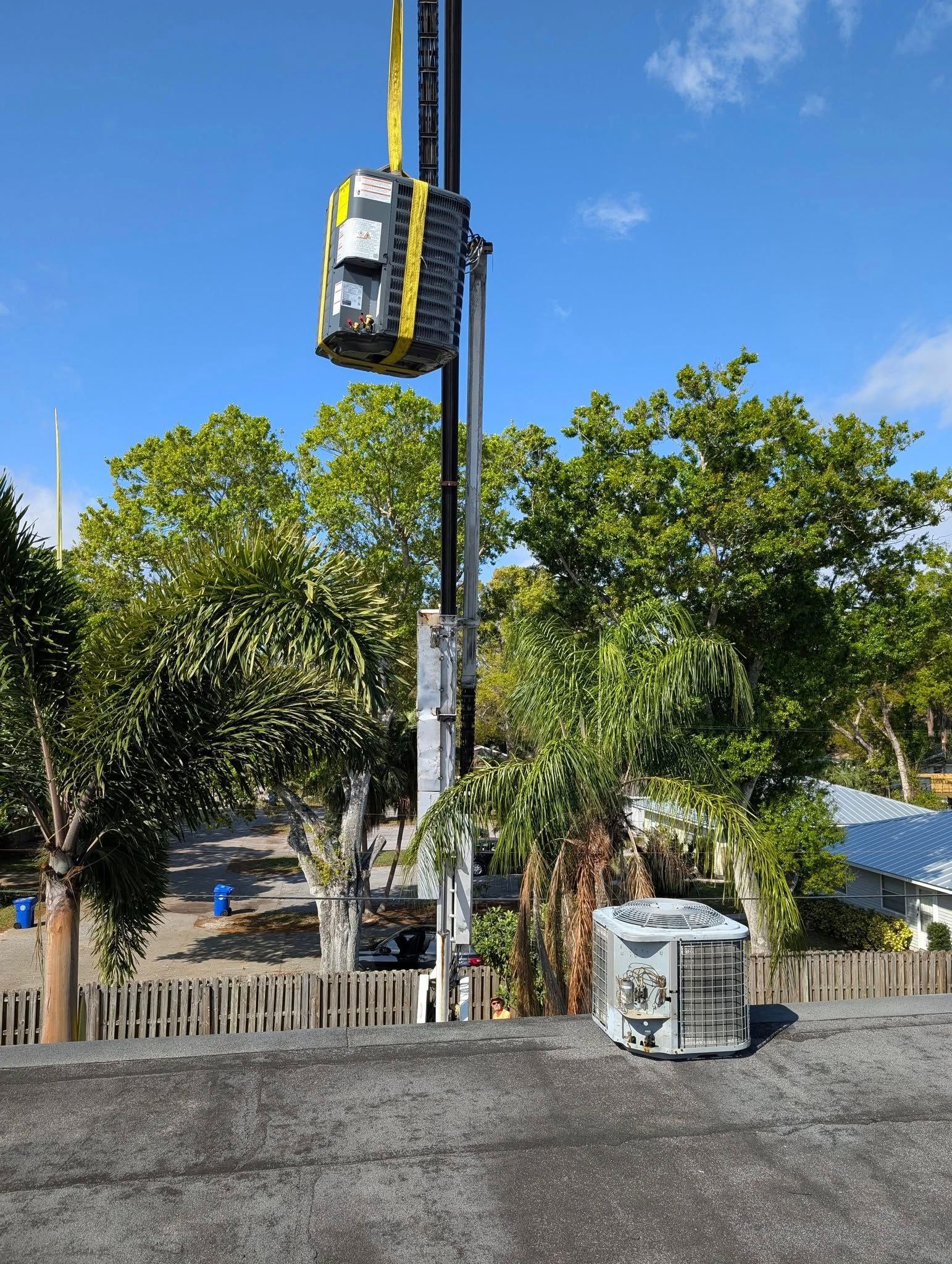 A crane is hanging from a pole in a parking lot with trees in the background.