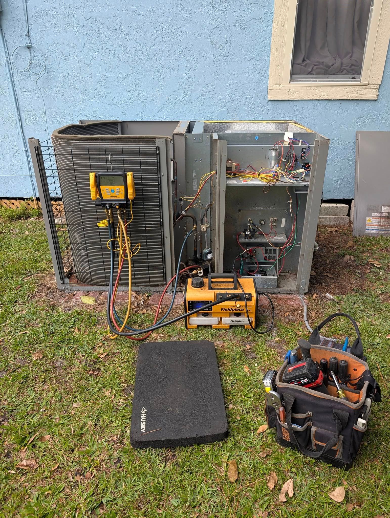 An air conditioner is being repaired in the backyard of a house.