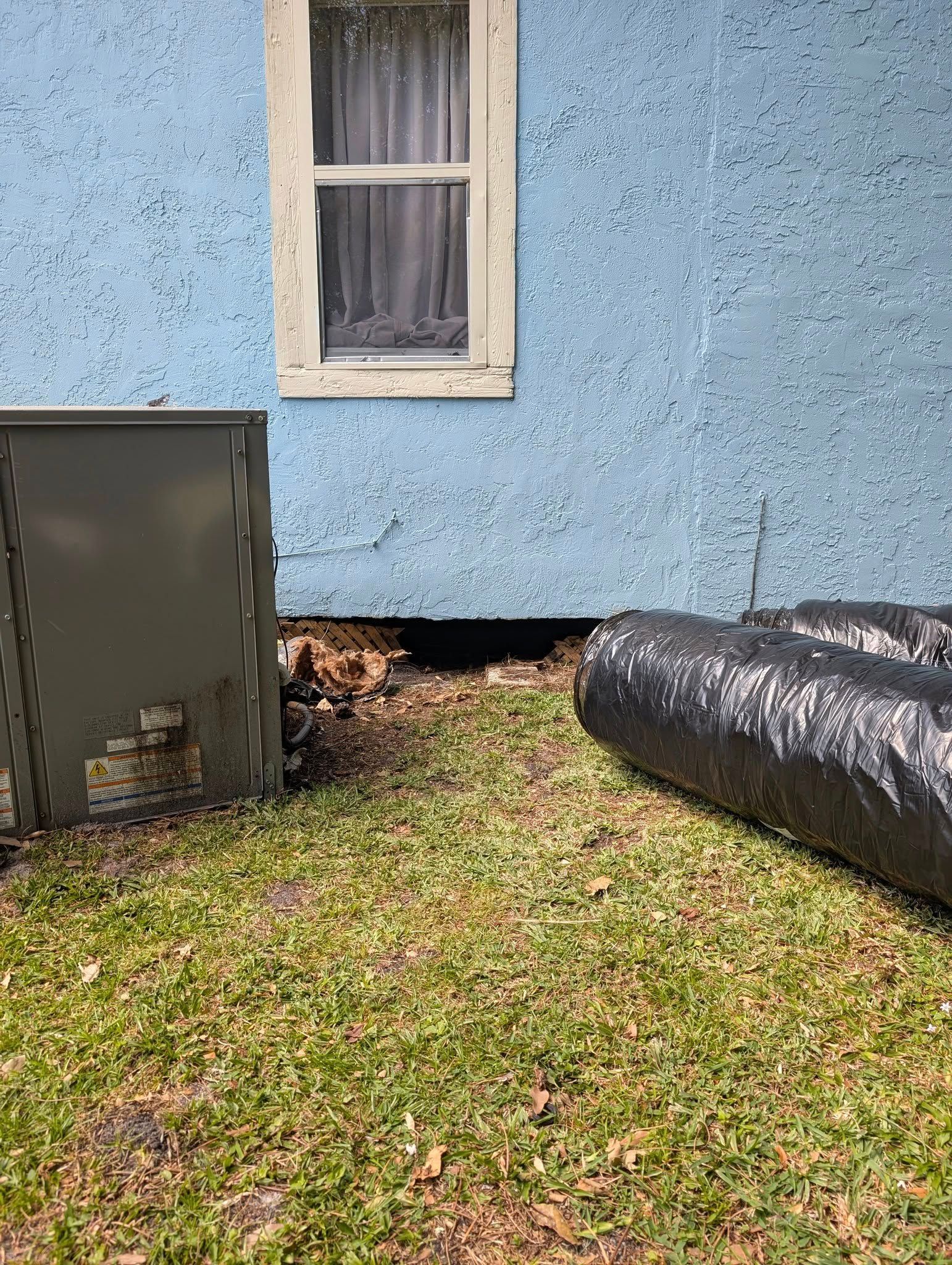 A blue house with a window and a black bag in front of it.
