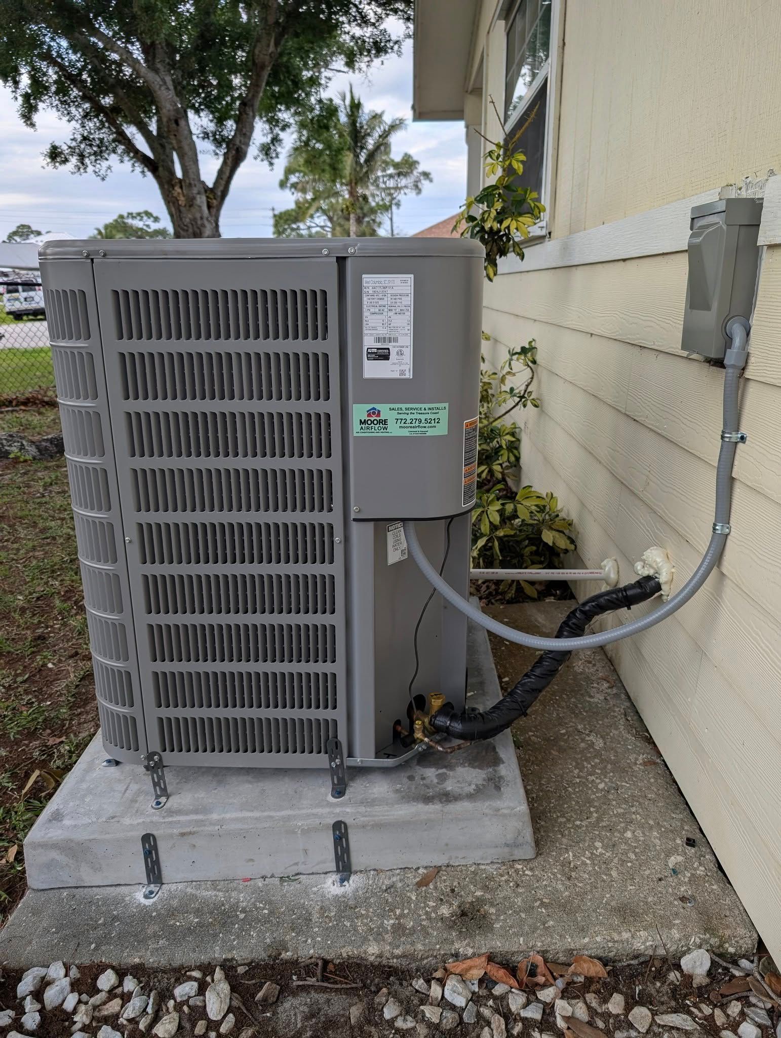 A gray air conditioner is attached to the side of a house.