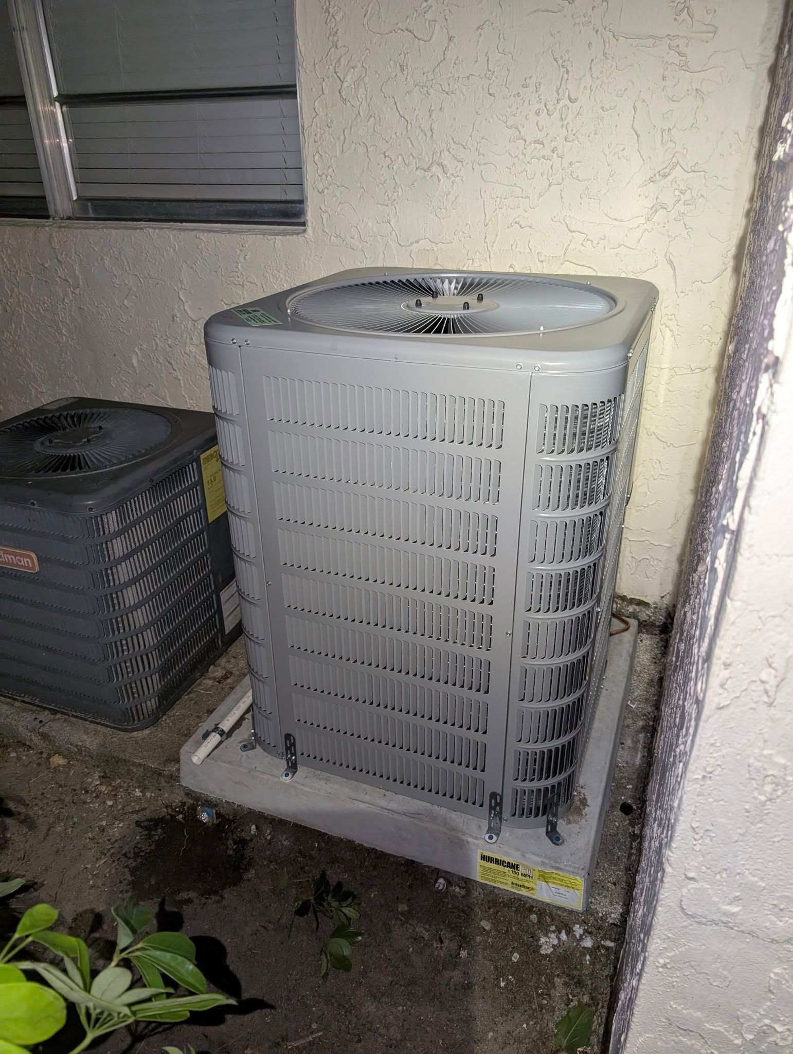 Two air conditioners are sitting next to each other on the side of a building.