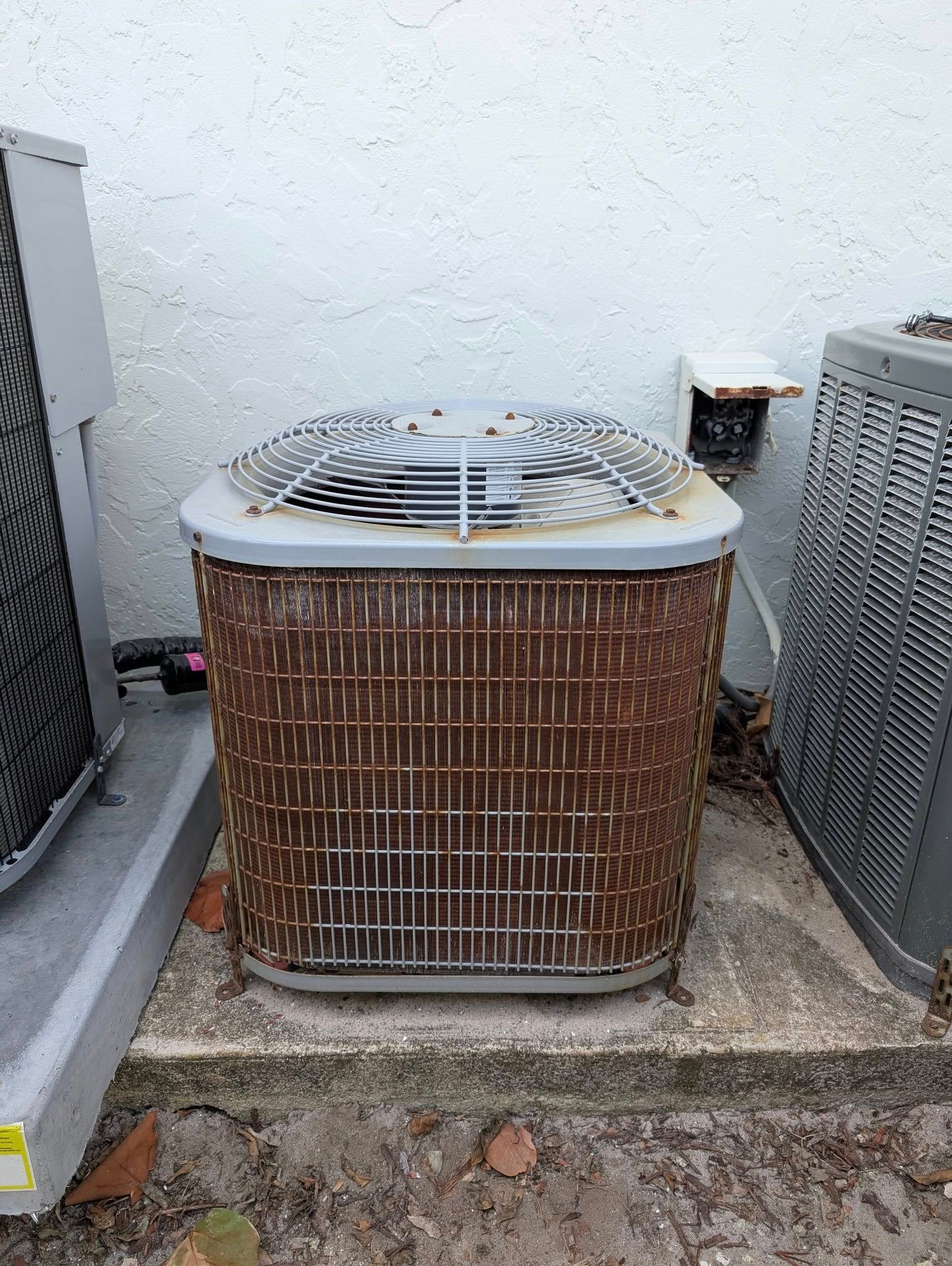 A dirty air conditioner is sitting on the ground next to a wall.