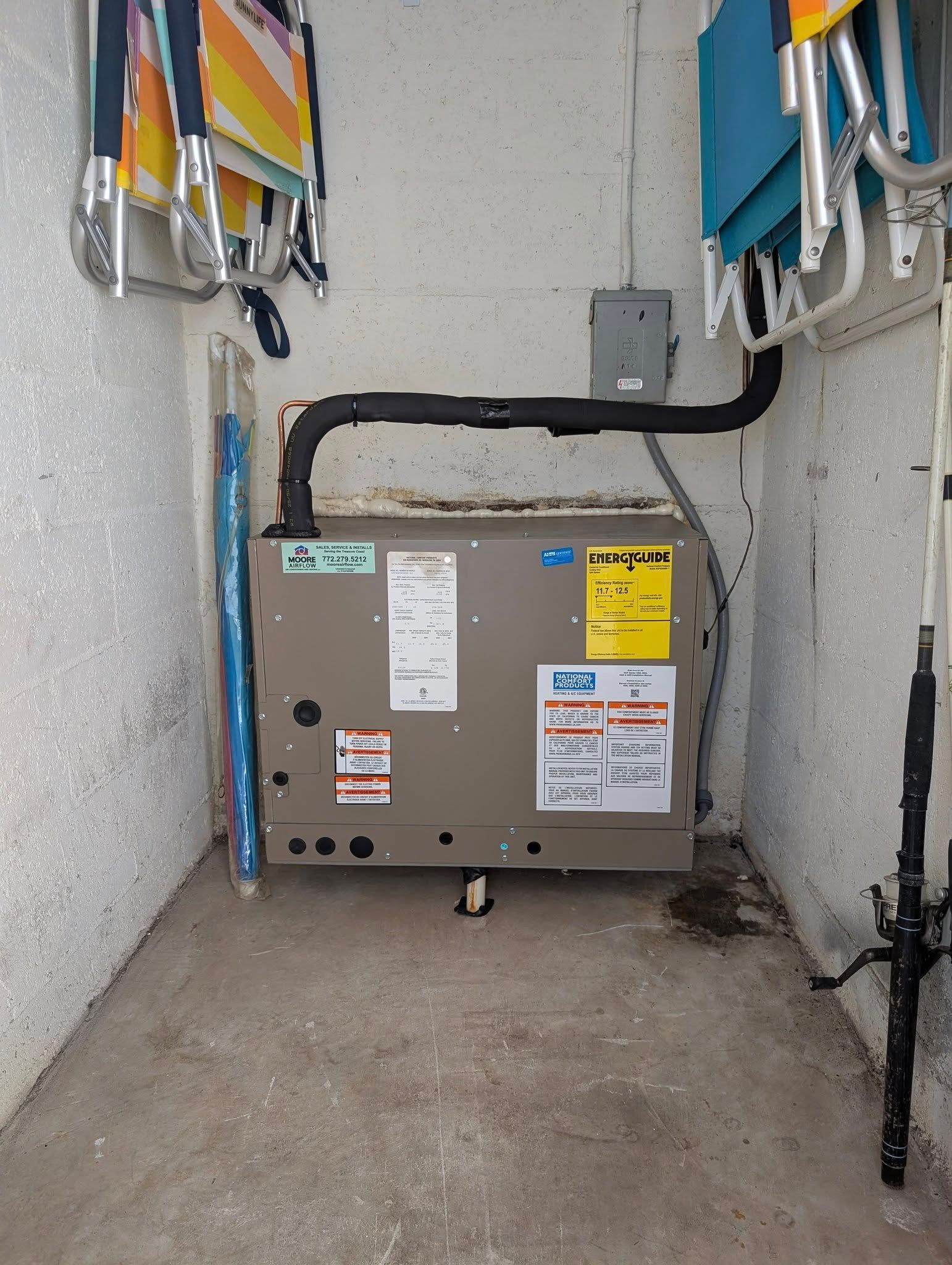 An air conditioner is sitting in a corner of a room next to beach chairs.