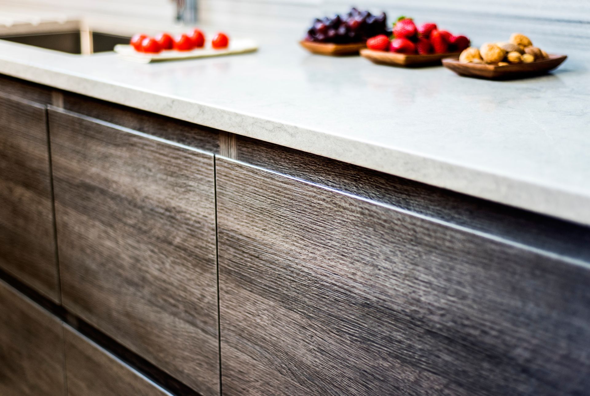 Dark wood kitchen cabinets with a light gray countertop, topped with bowls of fruit.