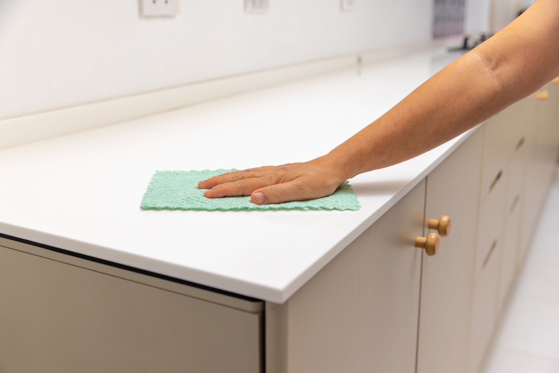 Hand wiping a white countertop with a green cloth in a kitchen.