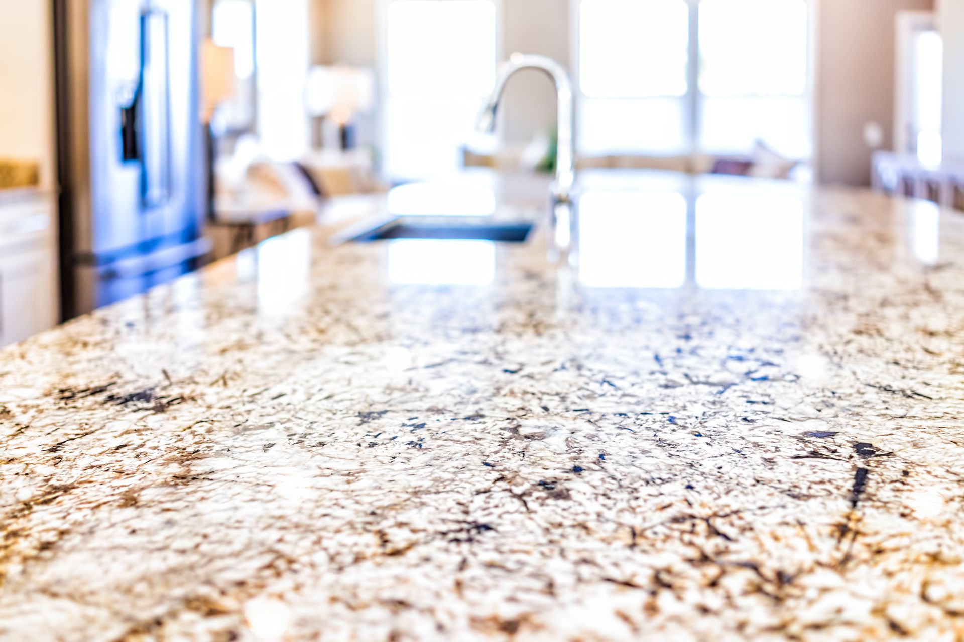 Close-up of a polished granite kitchen countertop with a sink in the background.