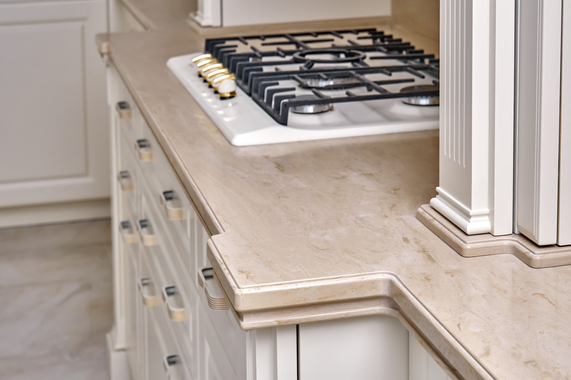 Beige marble countertop with a built-in gas stove and white cabinets in a kitchen.