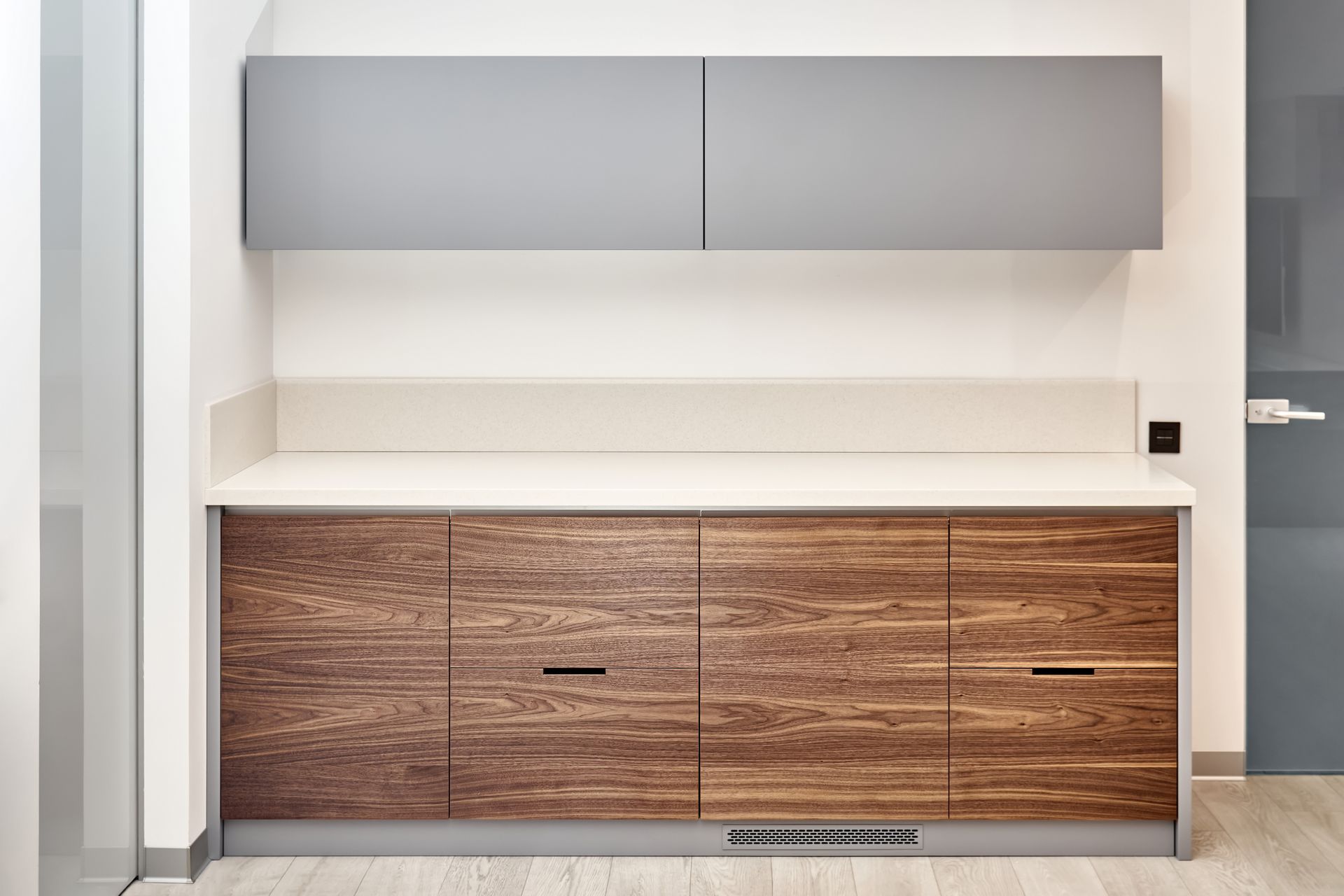 Wooden cabinet with countertop and gray upper cabinet against a white wall.