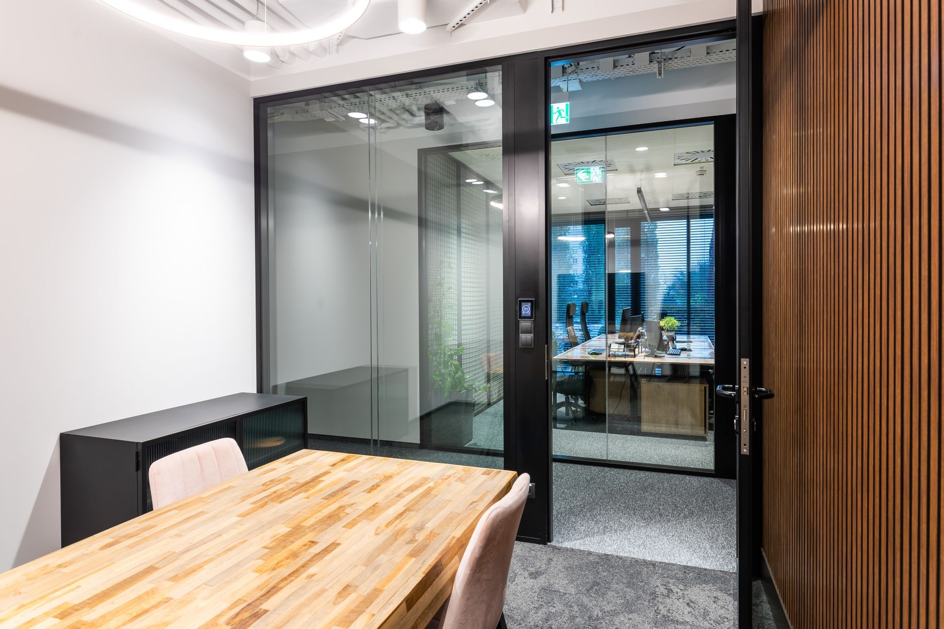 Office meeting room with wooden table, glass doors, and view to a work area.