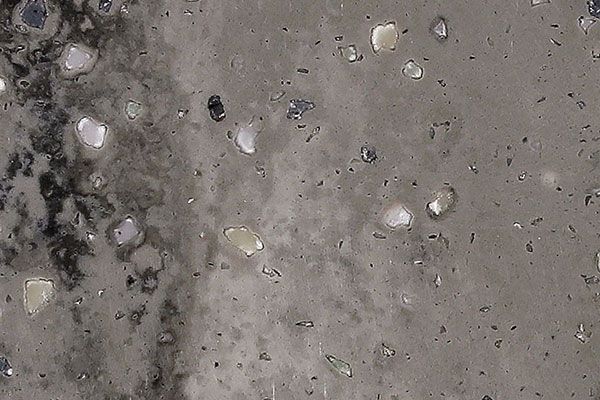 Gray concrete surface with embedded light-colored stones and dark, mottled areas.