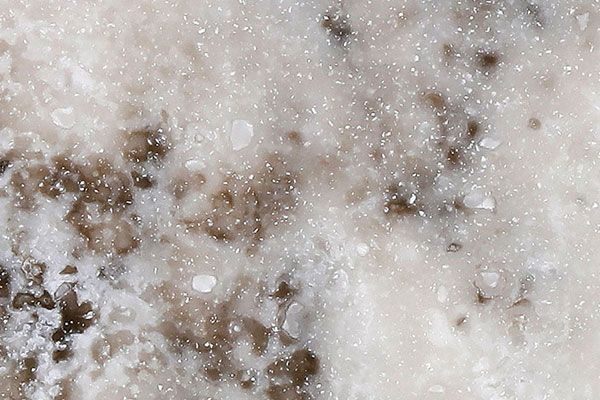 Close-up of a white marble surface with scattered brown and gray spots, and small water droplets.