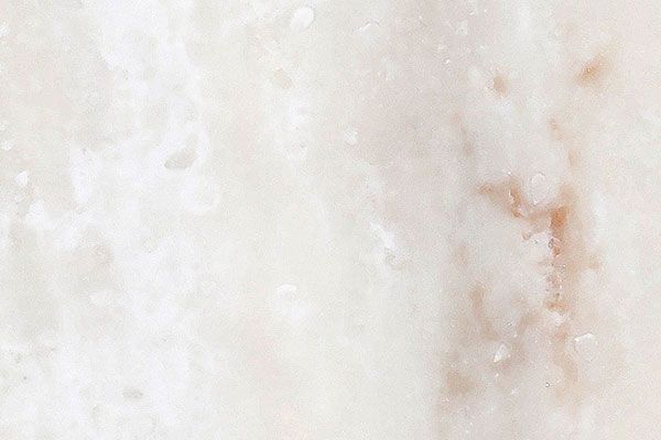 White and beige marble surface with swirled patterns and variations in color.