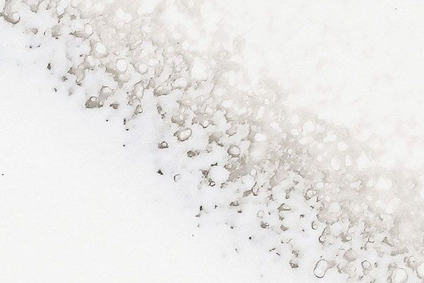 Textured off-white surface with a diagonal band of small, irregular dark gray shapes.