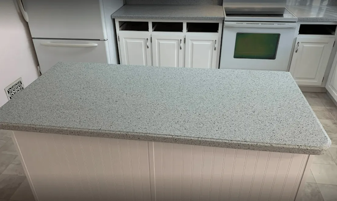 Kitchen island with gray speckled countertop, white cabinets, and appliances.