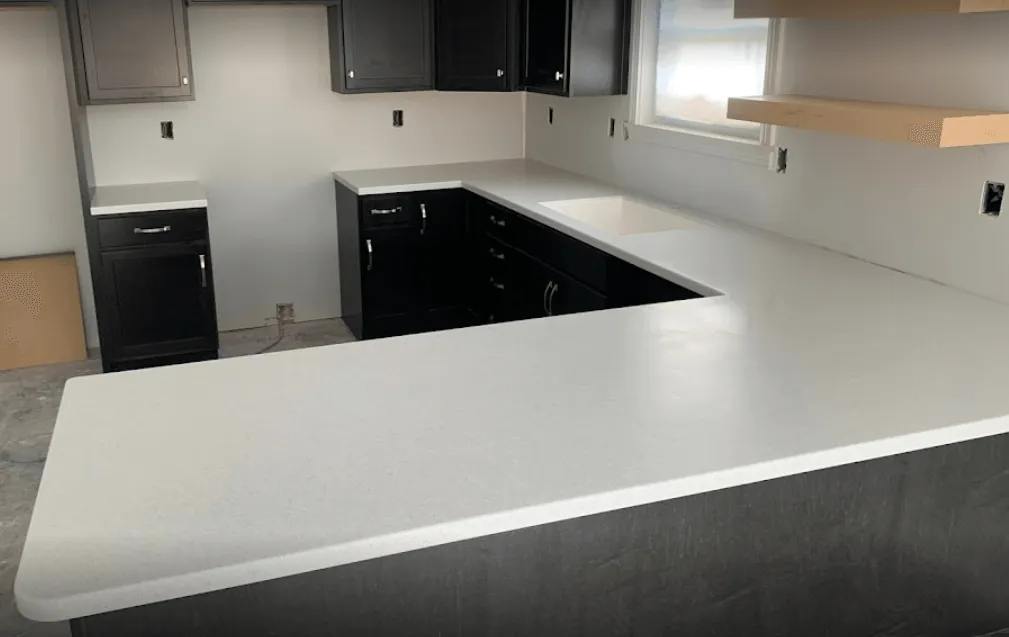 U-shaped kitchen with white countertops and black cabinets; window and floating shelves in the background.