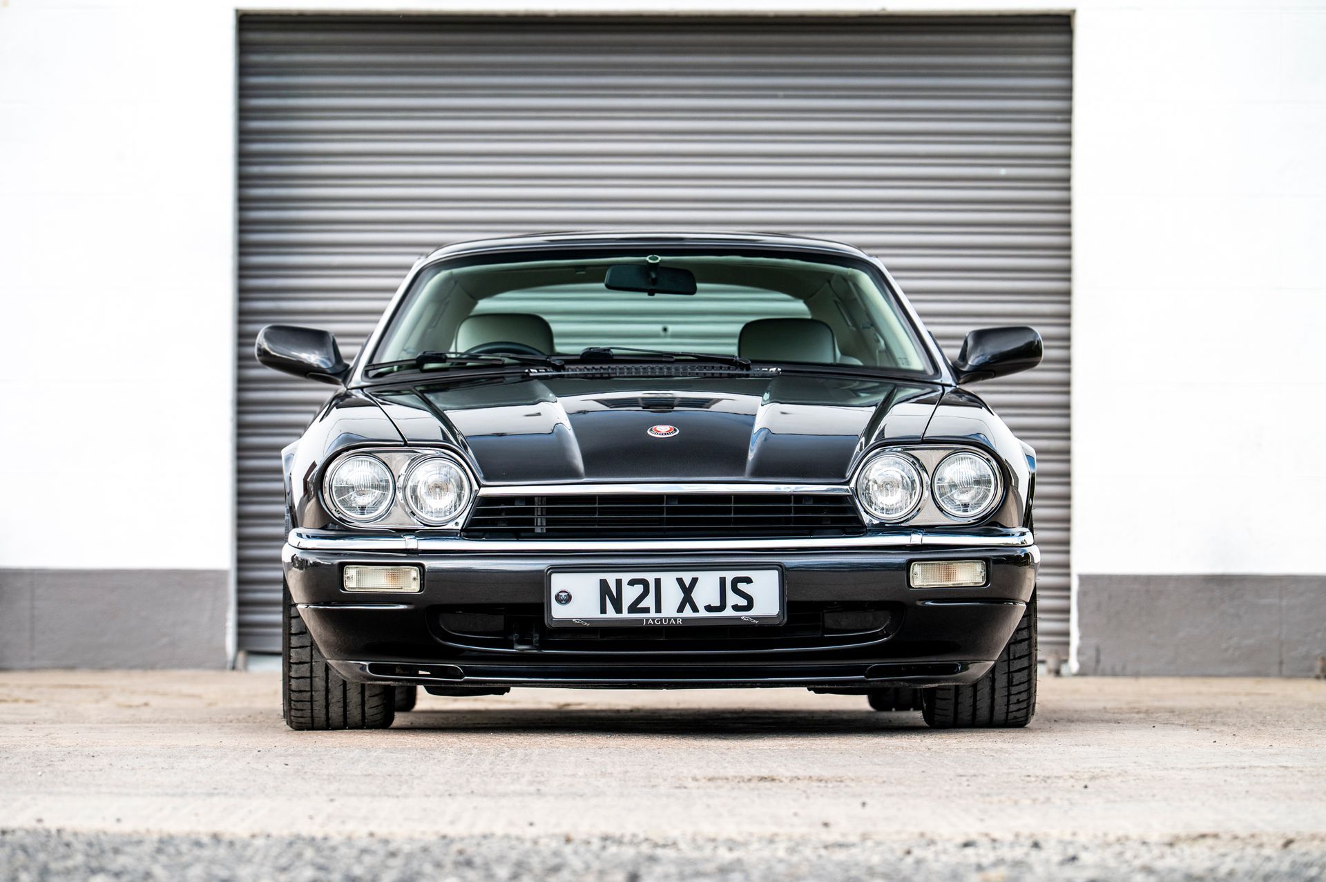 Black Jaguar XJS sports car parked in front of a closed garage door.