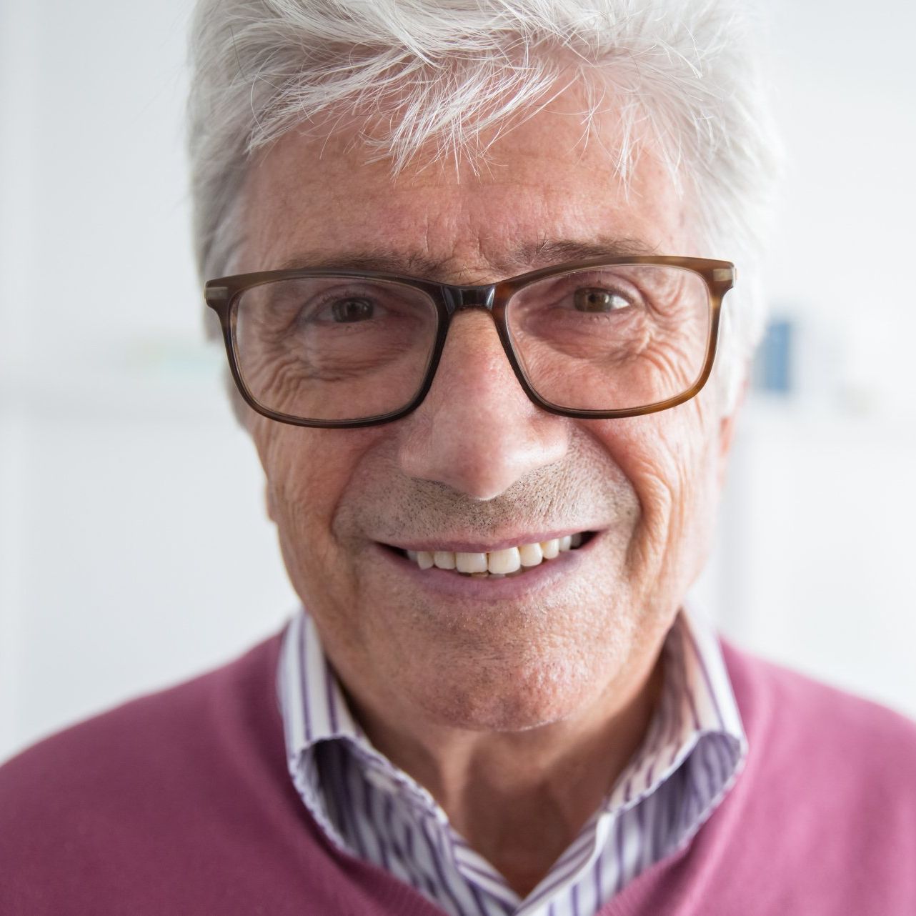 A man wearing glasses and a pink sweater smiles for the camera