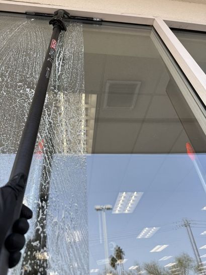 Window cleaner using a black squeegee on a glass storefront window with reflections of the sky and building.