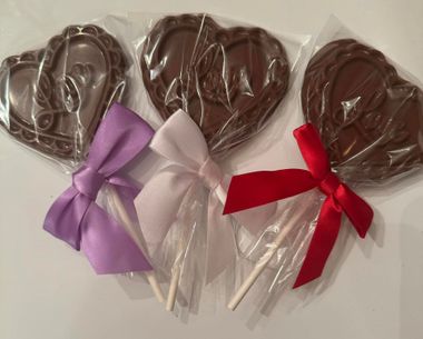 Three chocolate lollipops with lavender, white, and red bows on white sticks