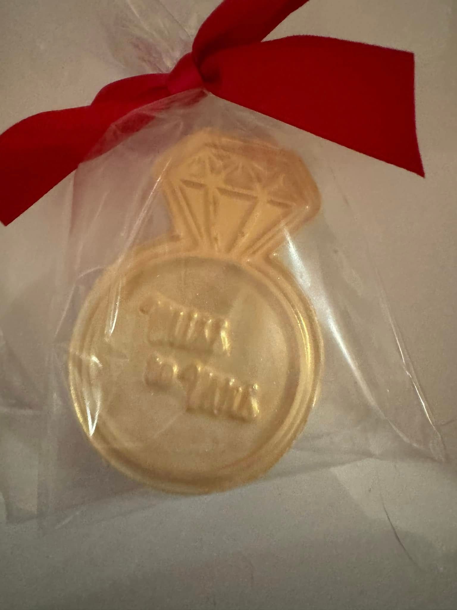 Gold medal-shaped ornament in a sheer bag, tied with a red ribbon.