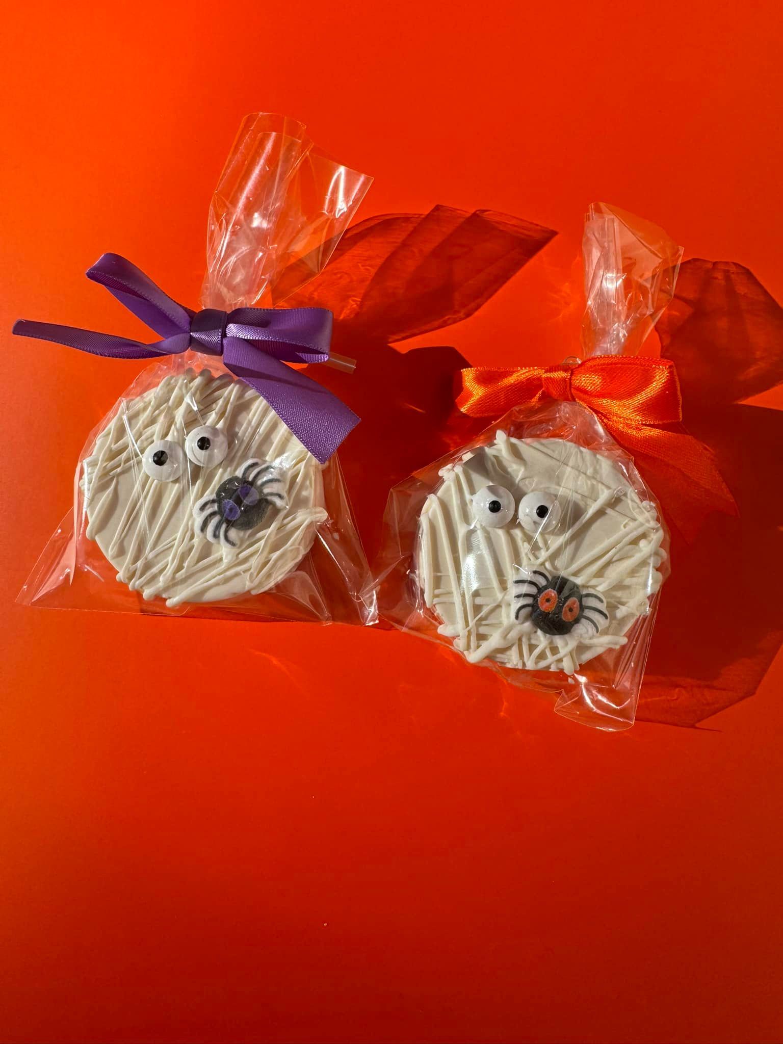 Two handmade candy treats wrapped in clear cellophane with purple and red bows on an orange background