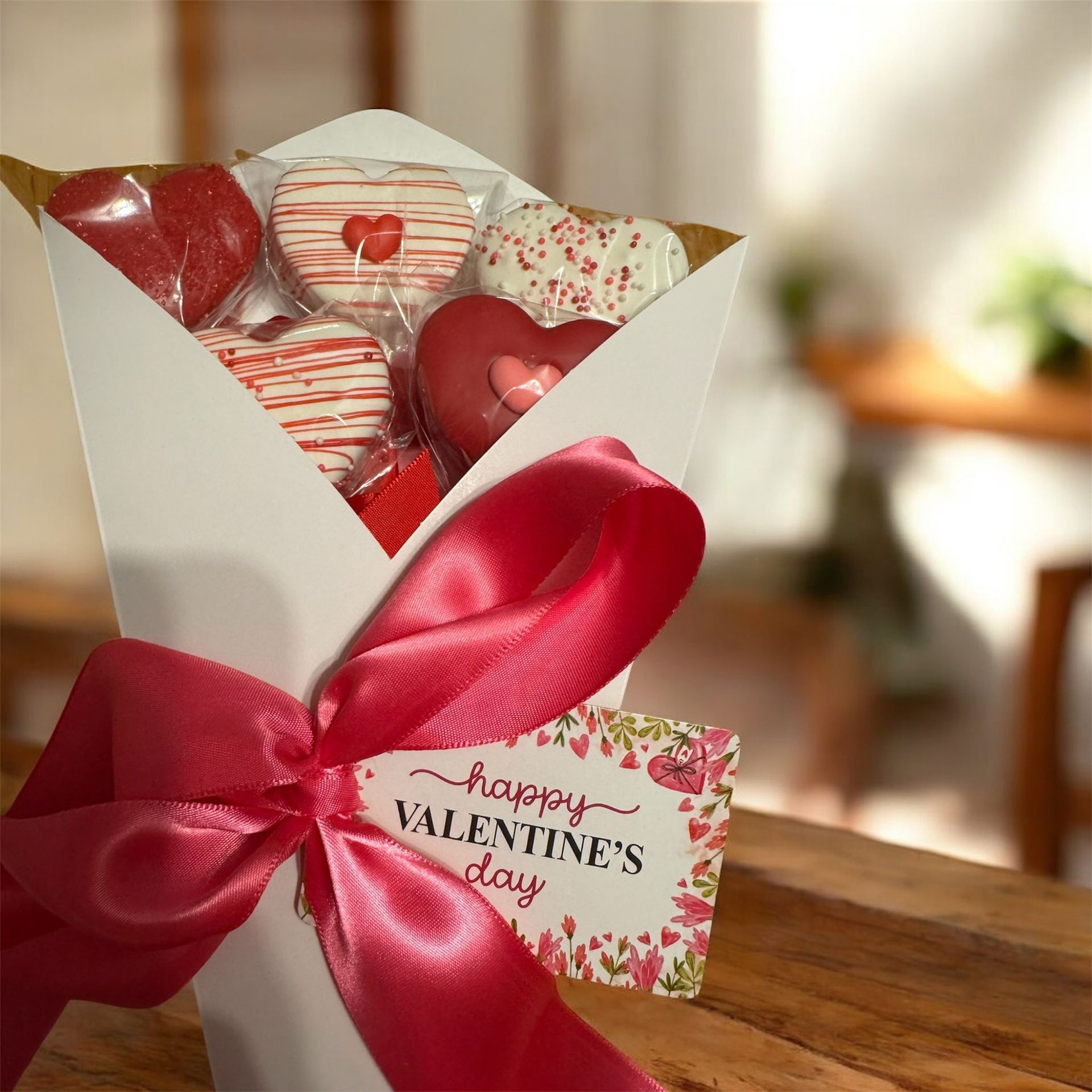 Heart-shaped Valentine gift box with red and striped candies, wrapped in a red ribbon and tag on a wooden table