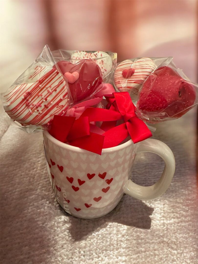 Heart-print mug filled with red ribbon, with wrapped heart-shaped candies behind it on a soft pink surface