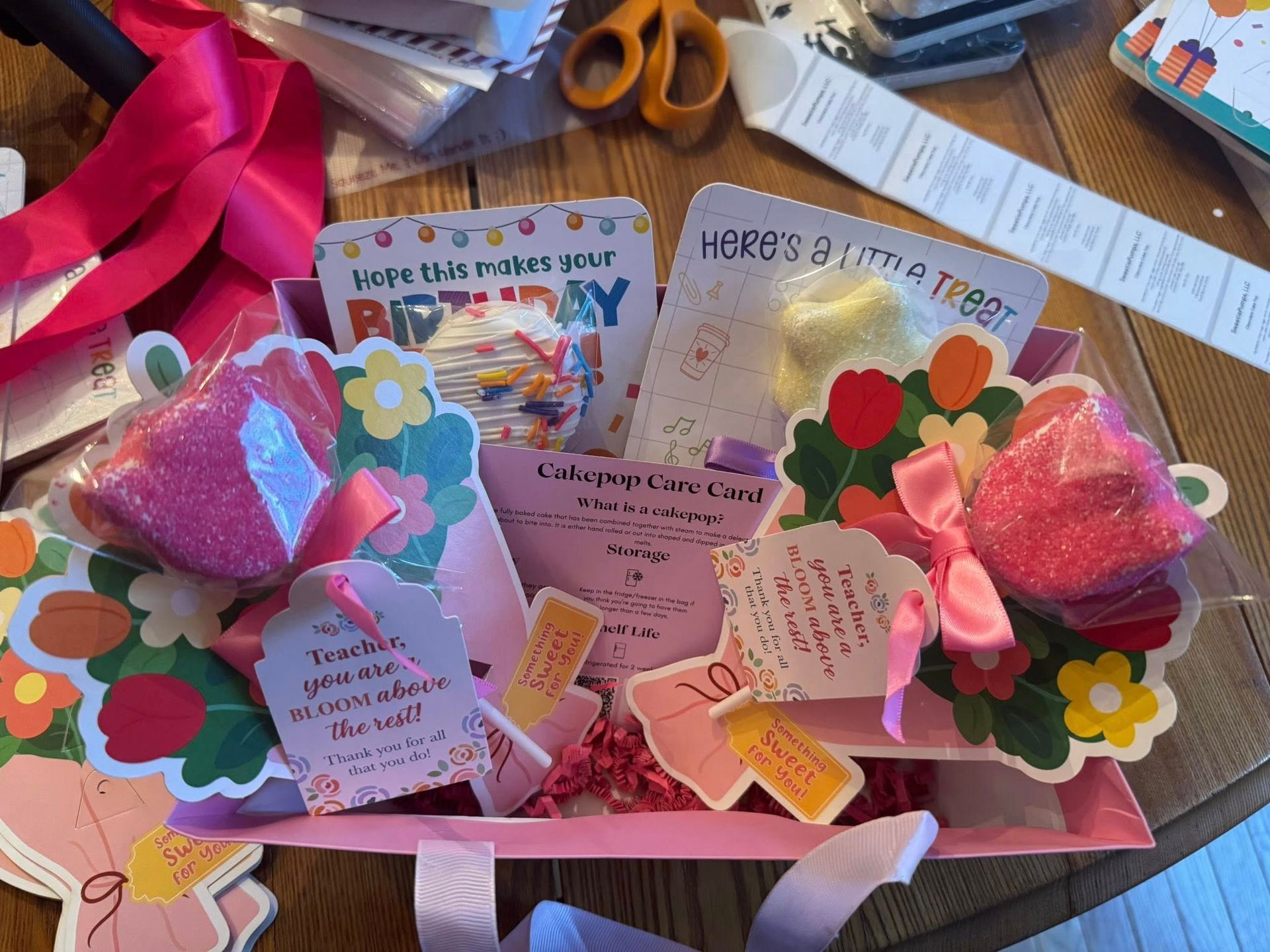 Pink handmade birthday card display with flowers, hearts, and gift tags on a desk