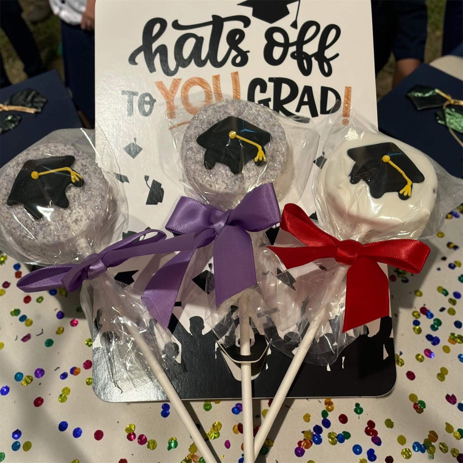 Graduation cupcake display with hats off to you sign, purple and red bows, and confetti table topper