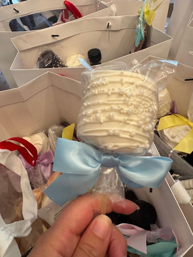 Hand holding a blue-ribboned white dessert treat in a box of similar wrapped treats