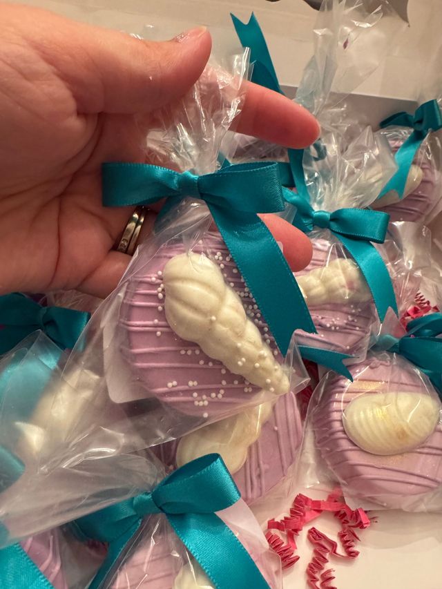 Hand holding teal-ribboned wrapped pink shell soaps or favors with white seashell accents