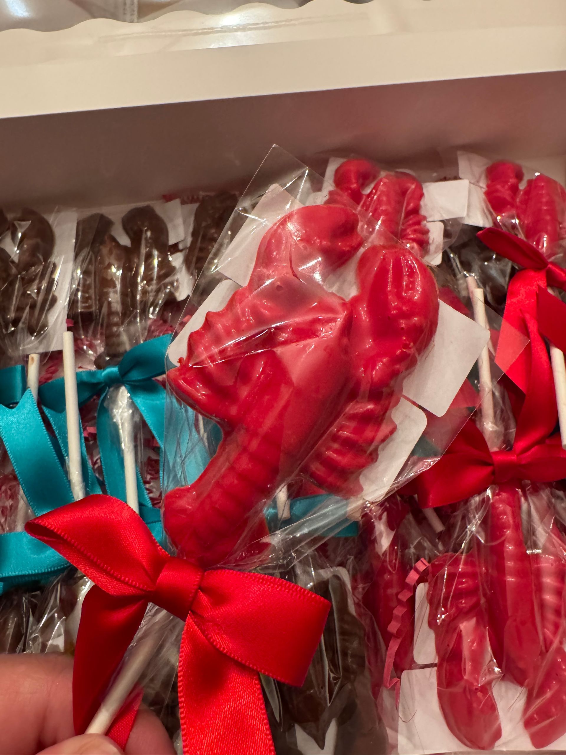 Red and teal ribbon-wrapped lollipops in a clear plastic package, held in a hand