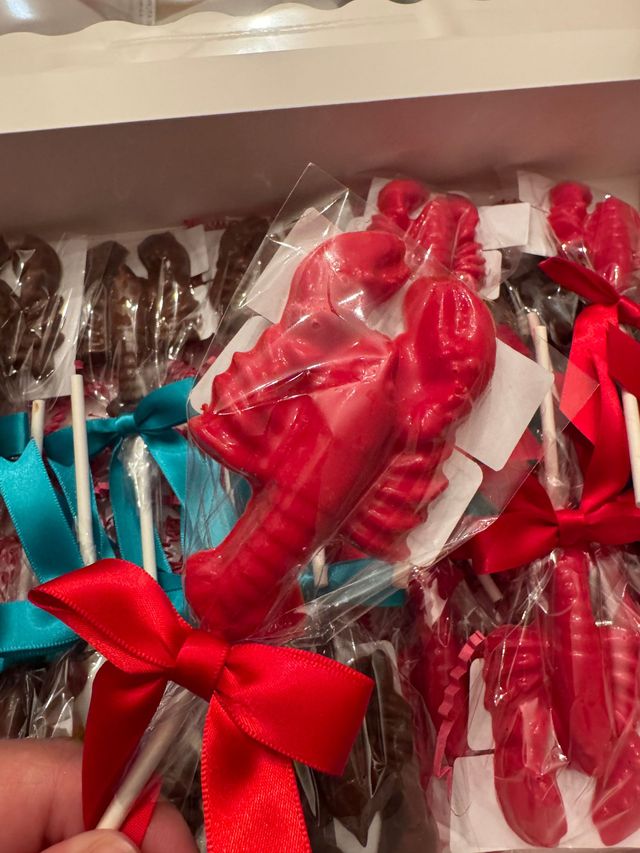 Red and teal ribbon-wrapped lollipops in a clear plastic package, held in a hand