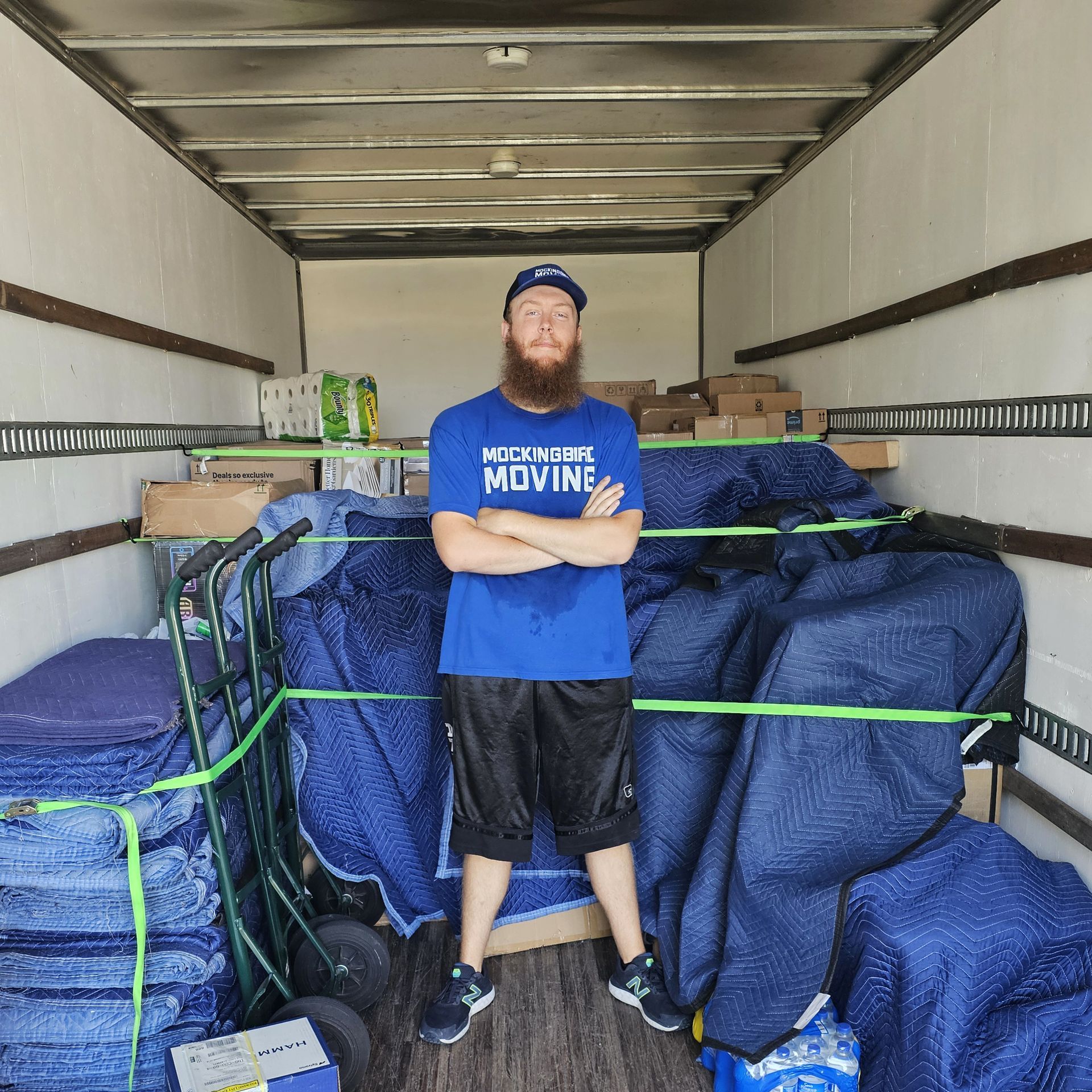 Two Men Are Carrying Boxes On A Dolly In A Living Room - Fayetteville, AR - Mockingbird Moving