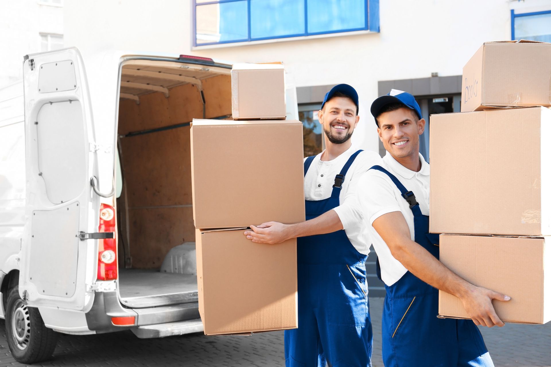 Two professional movers carrying stacked boxes from a delivery van outside a residential building