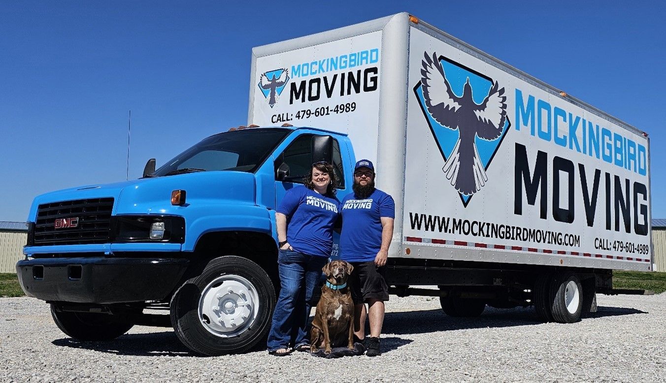 Two People And A Dog Are Standing In Front Of A Moving Truck - Fayetteville, AR - Mockingbird Moving
