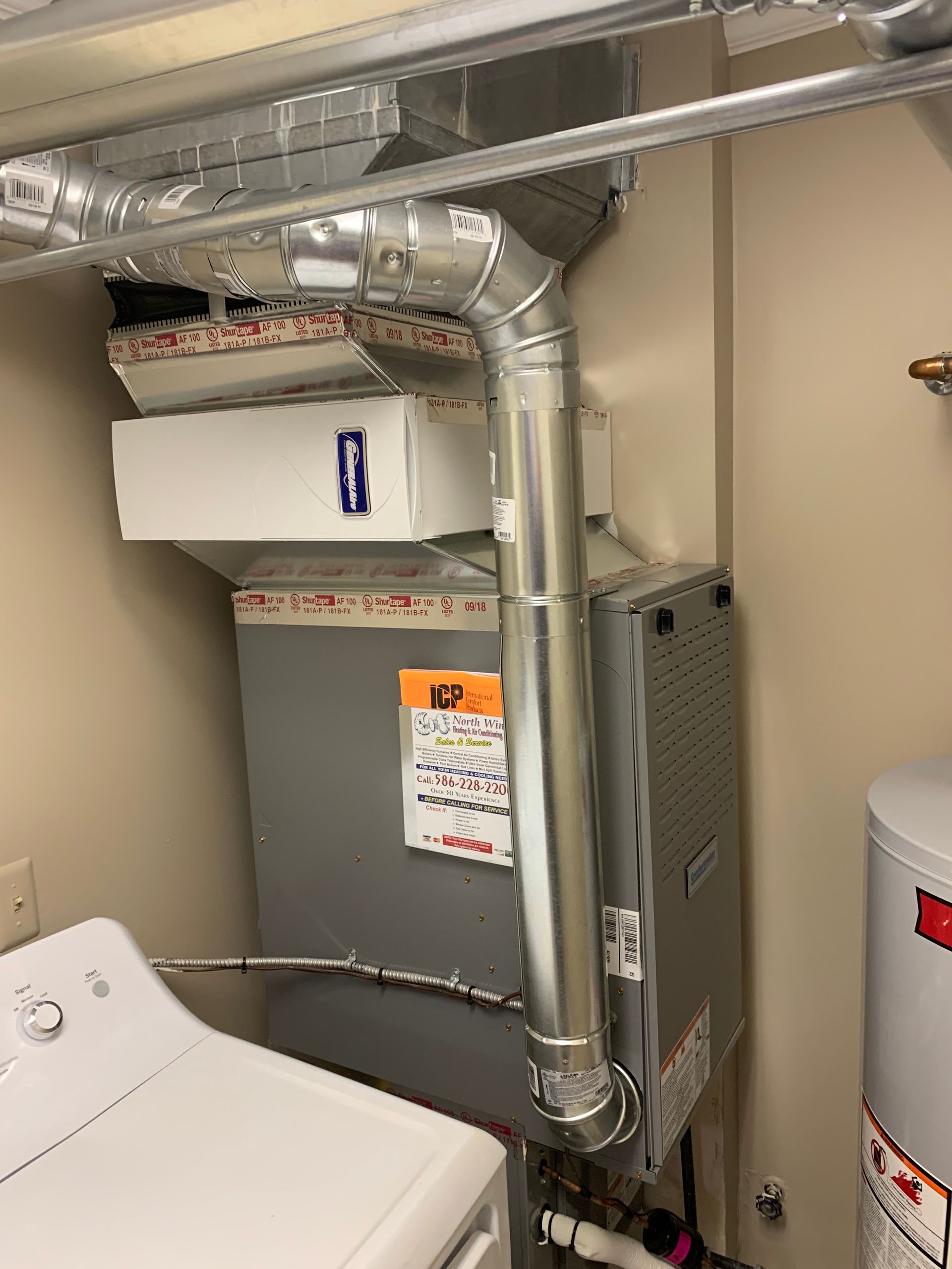 Furnace and air handler unit in a utility room, with ductwork and a water heater next to a washing machine.