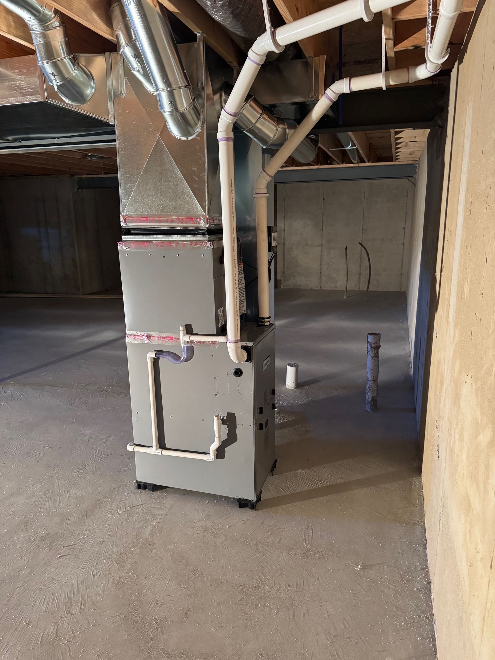 Attic HVAC furnace with exposed ductwork and pipes in an unfinished interior space