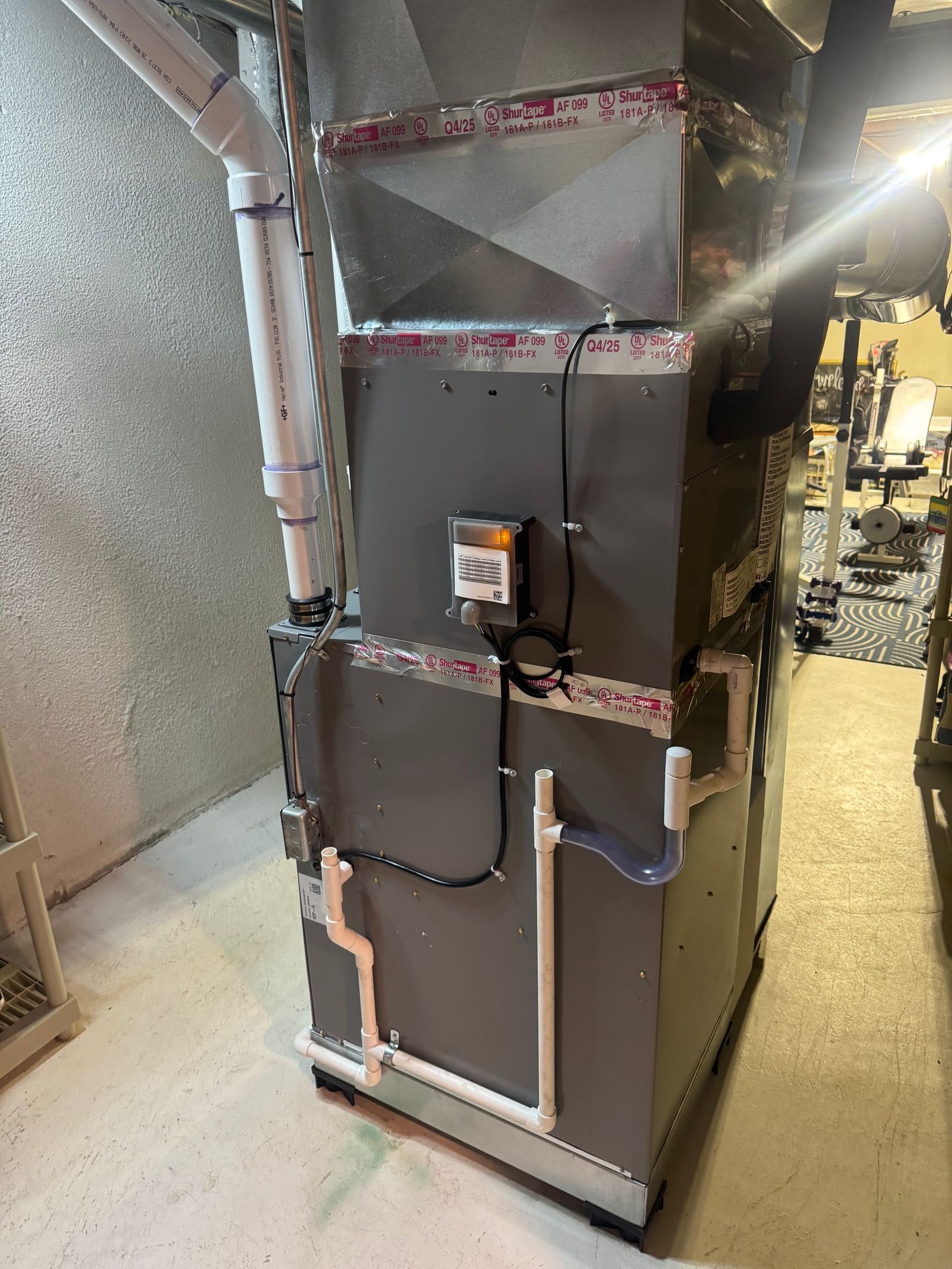 Wrapped HVAC unit in a basement or utility room with duct insulation and a control panel on the front