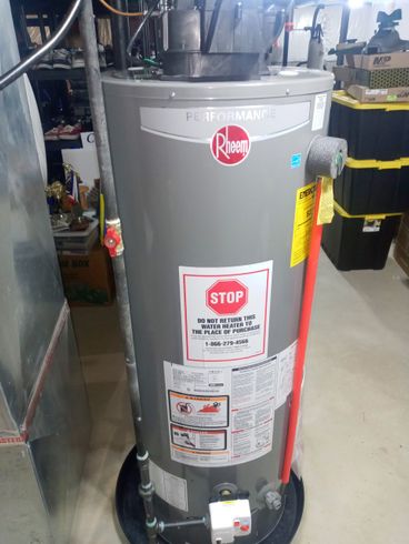 Gray Rheem water heater with red and black pipes in a utility room.