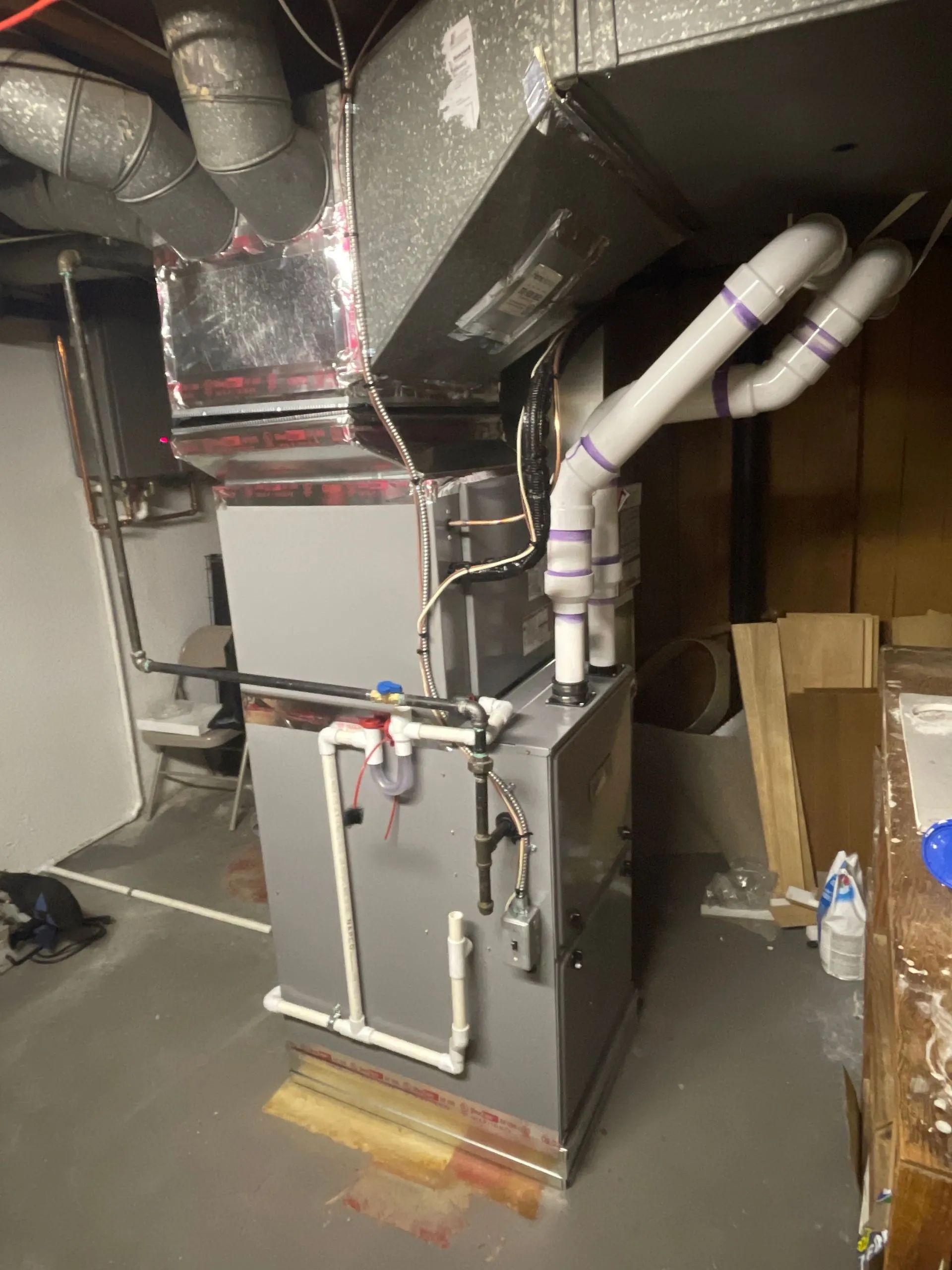 Large HVAC unit in a basement mechanical room with ductwork, pipes, and cardboard boxes nearby