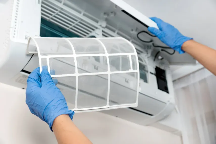 Hands in blue gloves removing an air conditioning filter from a wall unit.