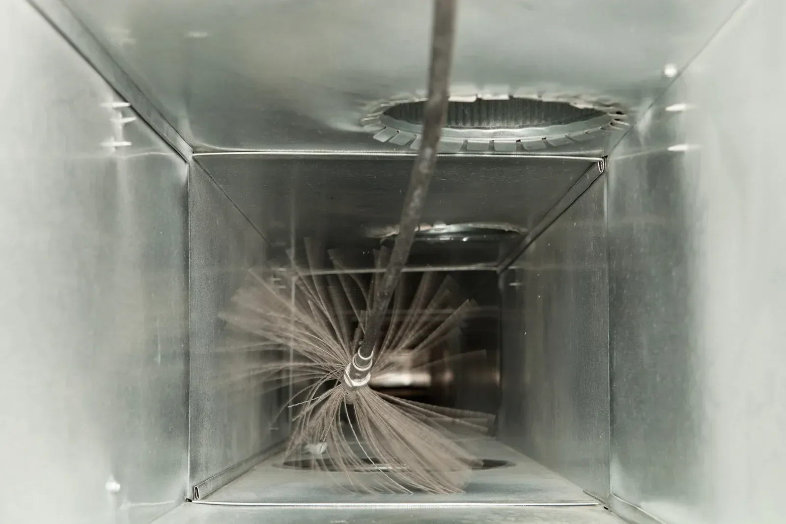Inside of a metal air duct being cleaned with a rotating brush, visible dust.