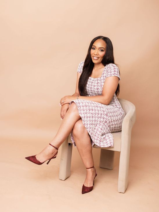 A woman is sitting at a desk with a laptop and a vase of flowers.