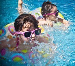 Two young girls wearing sunglasses are swimming in a pool.