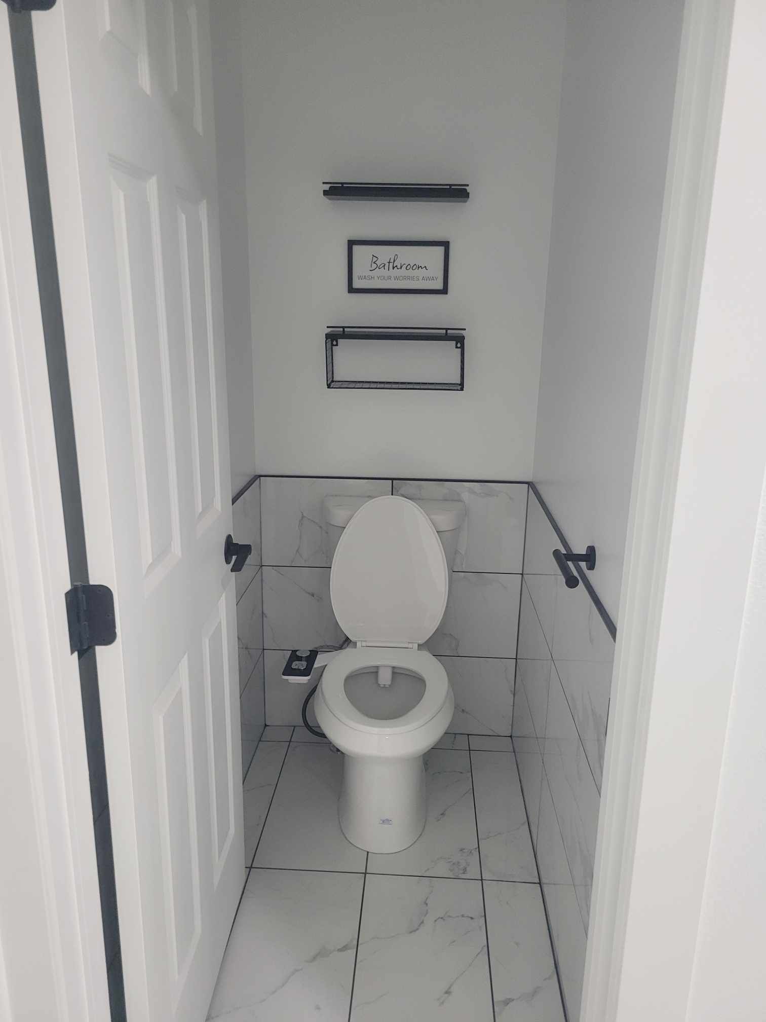 Small bathroom with a white toilet, tiled walls, and black fixtures.