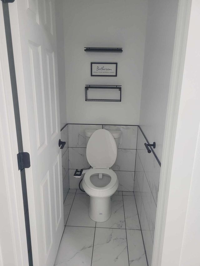 Small bathroom with a white toilet, tiled walls, and black fixtures.